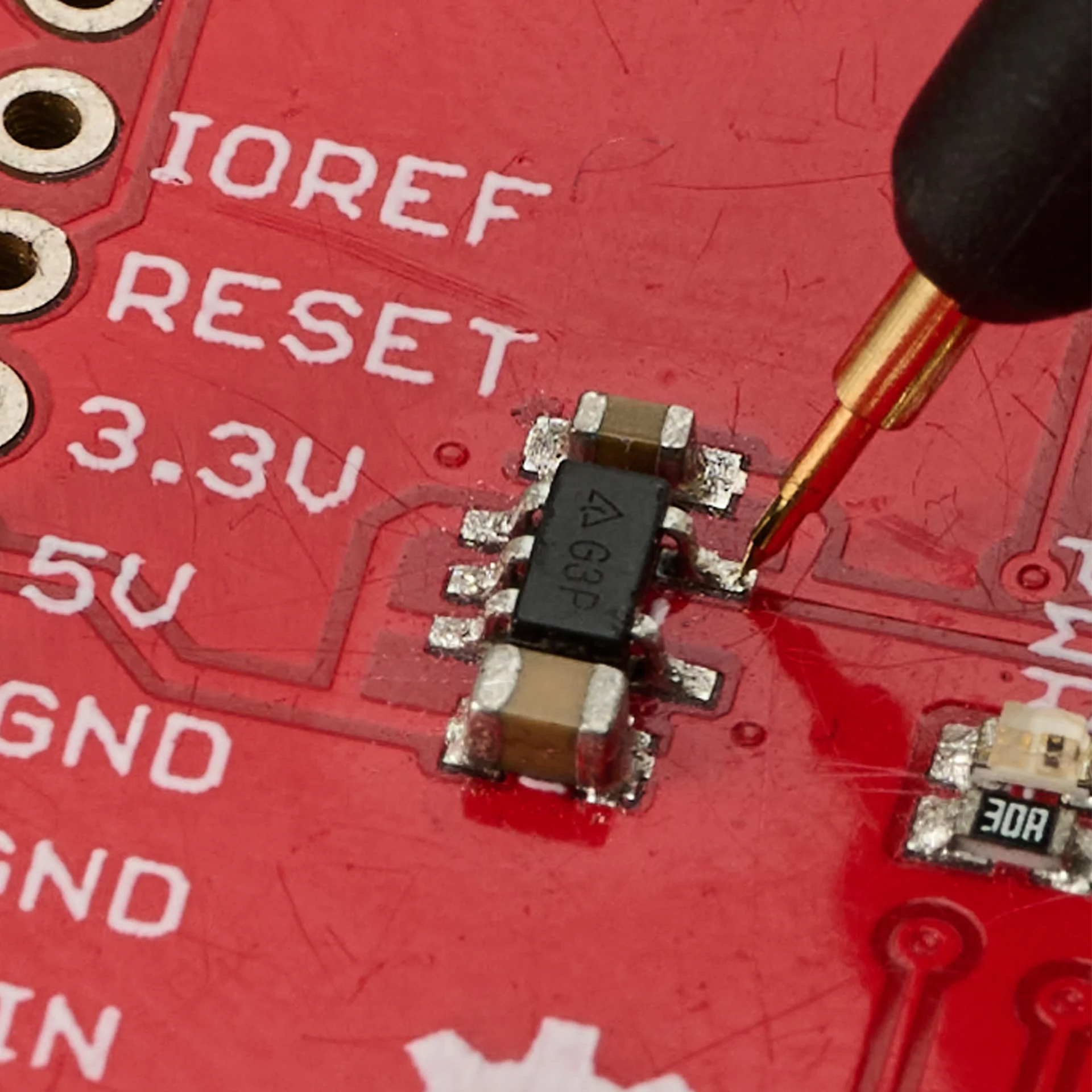 Gold-plated spring-loaded test needle resting on a pin of a small SMD chip, giving a stable low-resistance contact.