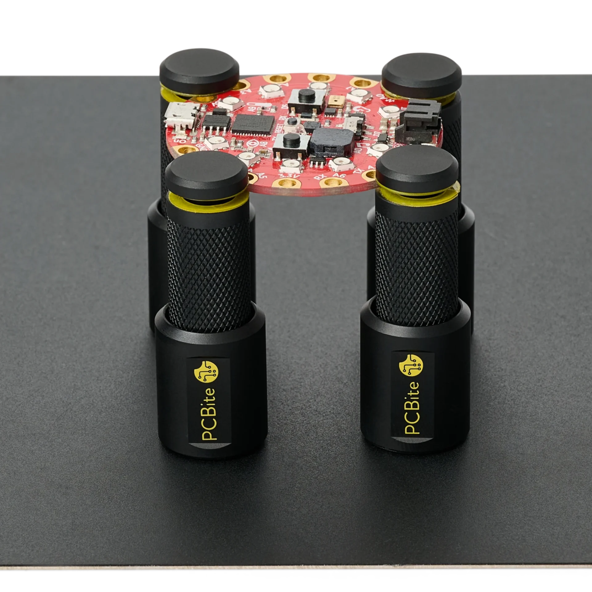 Four PCBite holders keeping a firm magnetic grip on an insulated base plate while holding a round PCB above it.
