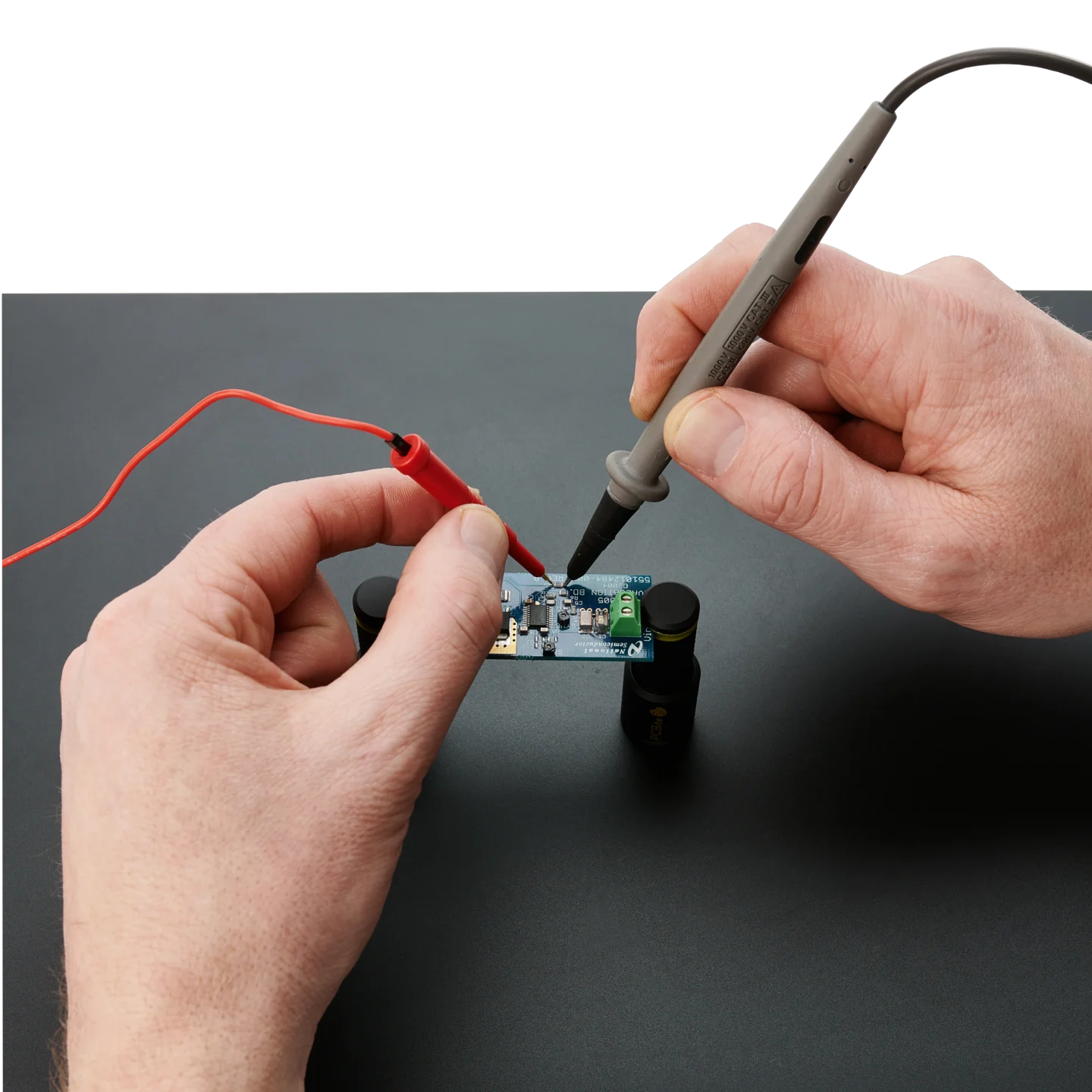 Hands holding and comparing a handheld SQ10 probe with a traditional larger multimeter probe (PCBITE-6011)