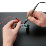 Hands holding and comparing a handheld SQ10 probe with a traditional larger multimeter probe (PCBITE-6011)