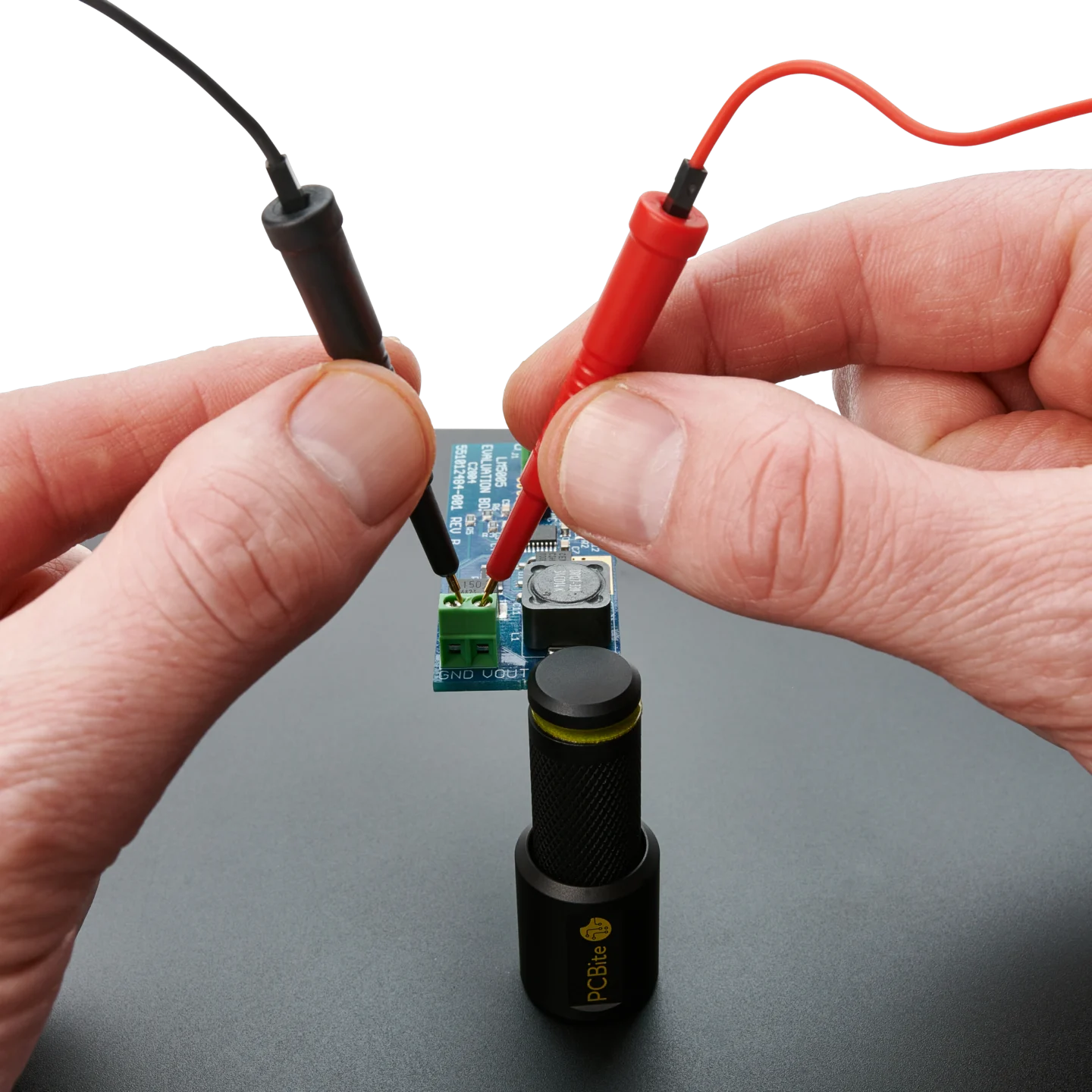 Hands holding two red/black SQ10 probes with spring-loaded tips on circuit board (PCBITE-6019)