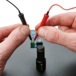 Hands holding two red/black SQ10 probes with spring-loaded tips on circuit board (PCBITE-6019)