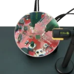 Two SQ350 350MHz oscilloscope probes measuring handsfree on PCB showing different grounding options through magnifier lens (PCBITE-6023)