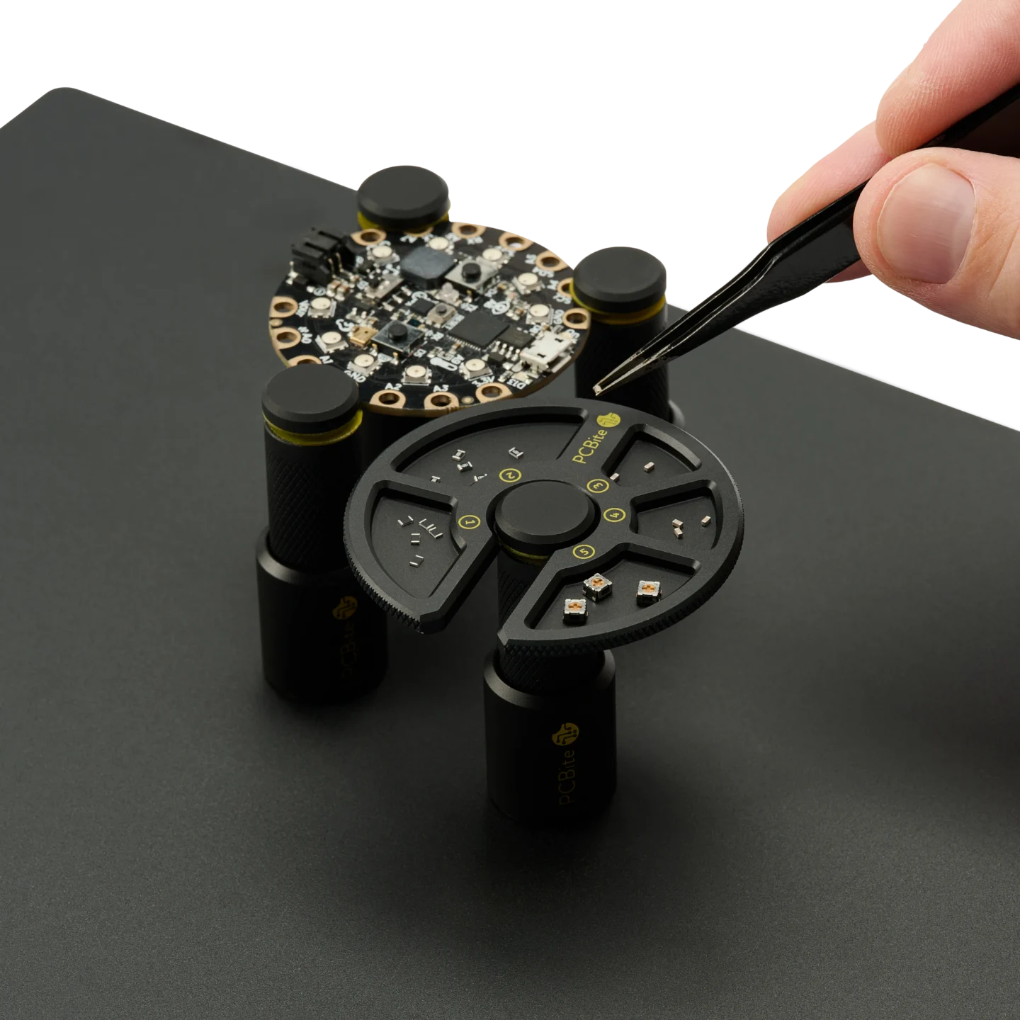 Hand picking components with tweezer from component tray and placing on PCB for soldering (PCBITE-7029)