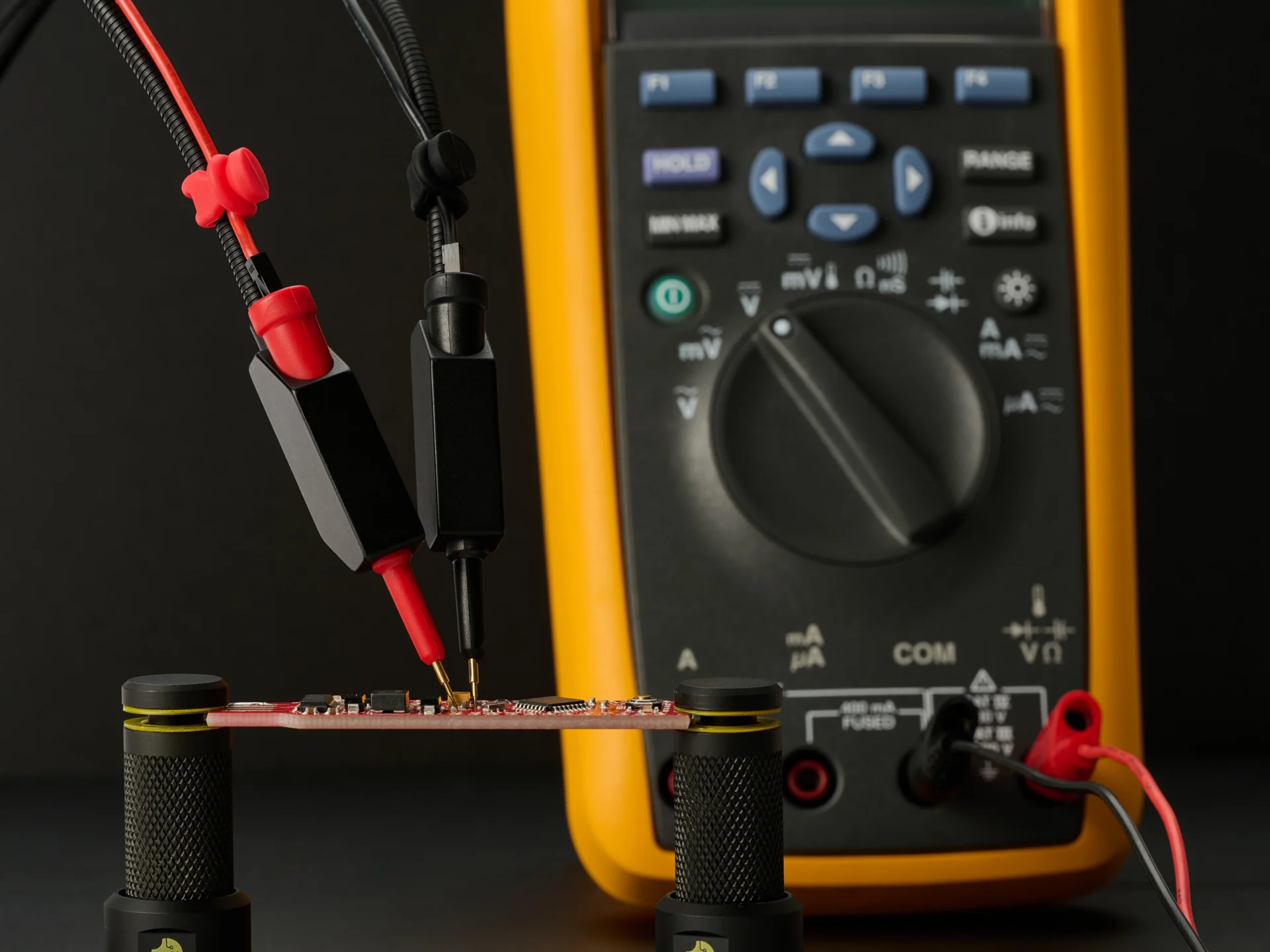 Red and black SQ10 probes resting on a PCB in PCBite holders, wired to a FLUKE multimeter so the readings need no hands.