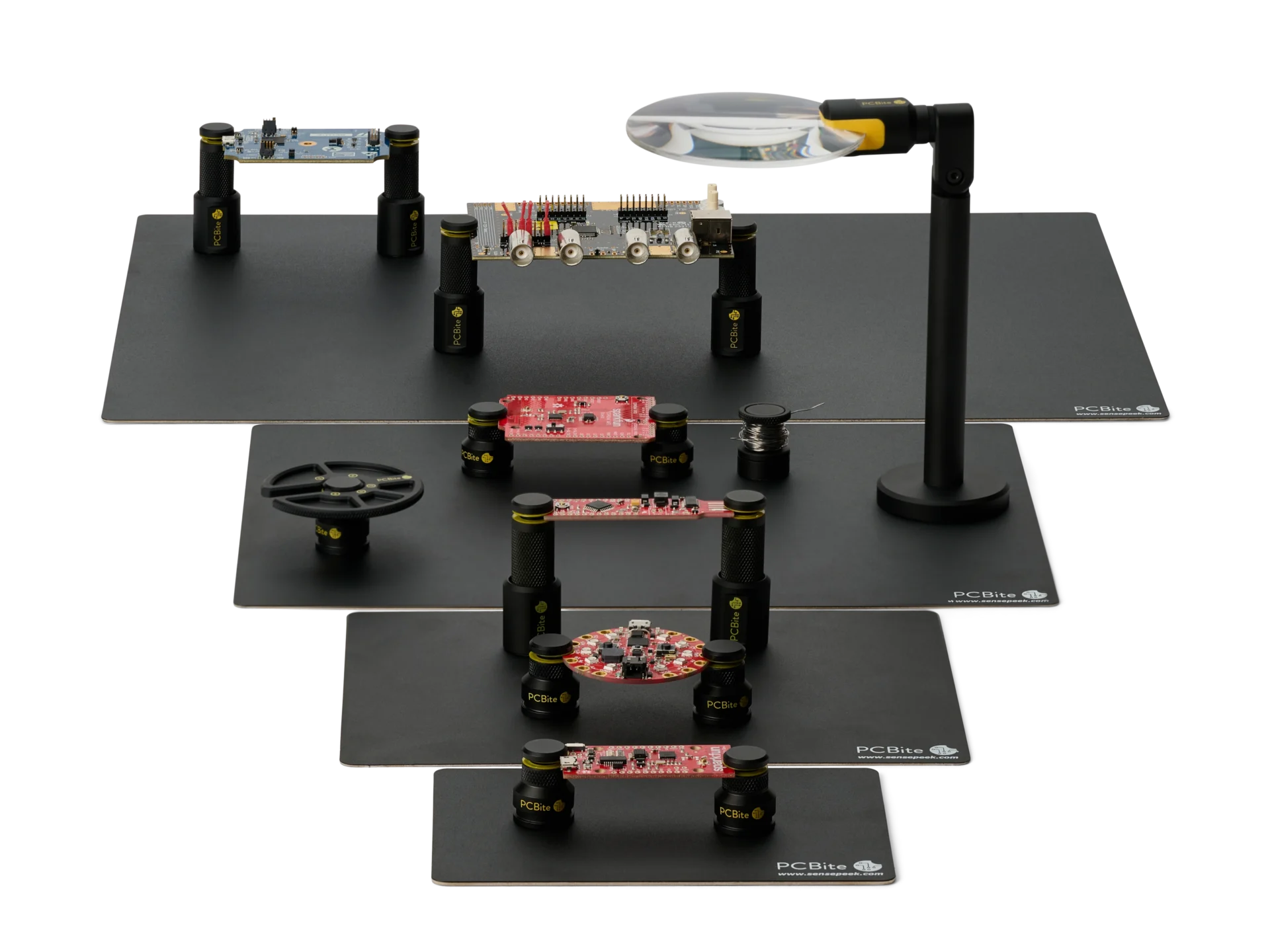 PCBite base plates from XS to XL, each with PCB holders on it, plus a magnifier, a component tray and a solder wire stand.