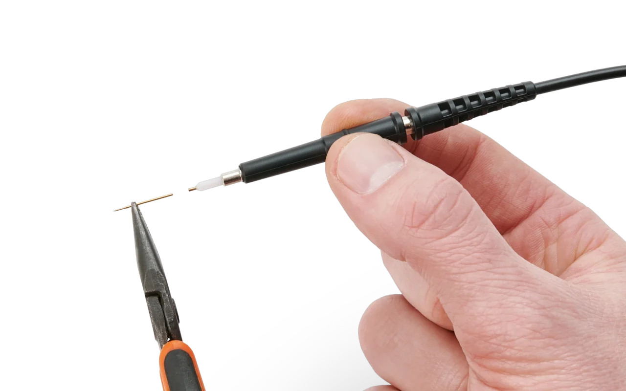 Oscilloscope probe held in one hand while pliers hold its spring-loaded test needle, showing how the needle is replaced.