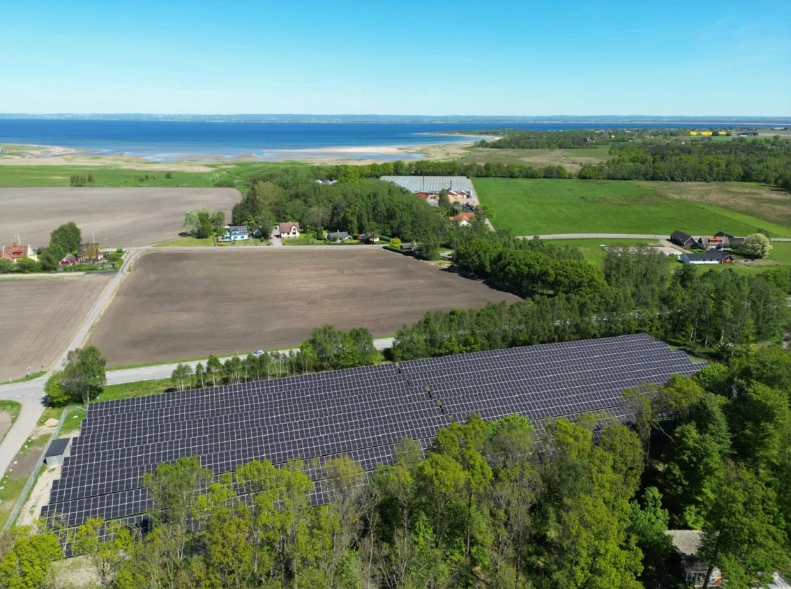 Aerial view of the ground-mounted solar park at Björkeröd outside Höganäs, with fields and the sea behind it.